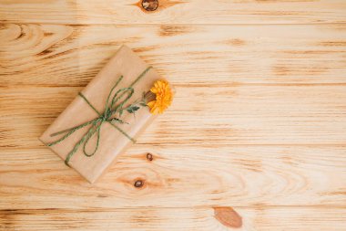 Çiçek arkaplan. Kahverengi kağıda sarılı bir hediye. Hafif ahşap arka planda sarı kasımpatı. Üst görünüm