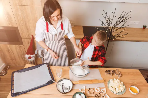 Mom and son are kneading dough for cookies at a wooden table in the kitchen. Cooking desserts at home. Joint activities with children. Top view