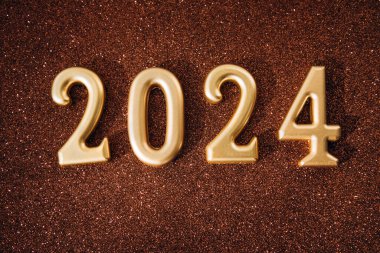 Boşluklu selamlama arkaplanı. Mutlu yıllar kartı. Kahverengi parlak arka planda 2024 altın figürleri. Üst görünüm
