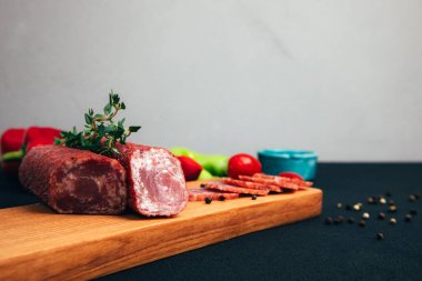 Yeşil kağıt ve domatesli ahşap tepside farklı tip ve boyutlarda sosis. Koyu ahşap arka planda tütsülenmiş sosis seti. Ön görünüm