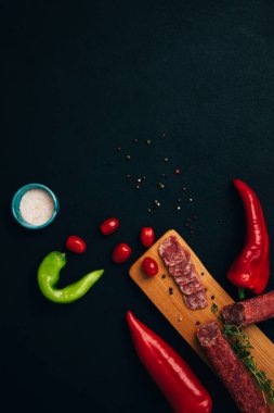 Yeşil kağıt ve domatesli ahşap tepside farklı tip ve boyutlarda sosis. Koyu ahşap arka planda tütsülenmiş sosis seti. Üst görünüm