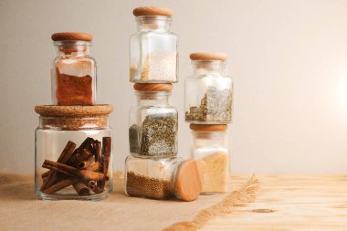 Hafif ahşap arka planda cam kavanozlarda bir grup baharat. Paprika, otlar, hardal, sarımsak, ön manzara, seçici odak