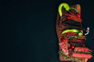 Yeşil kağıt ve domatesli ahşap tepside farklı tip ve boyutlarda sosis. Koyu ahşap arka planda tütsülenmiş sosis seti. Üst görünüm