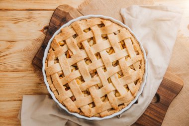 Elmalı turta açık ahşap arka planda kahverengi mutfak havlusuyla mavi formda. Hazır turta. Üst görünüm