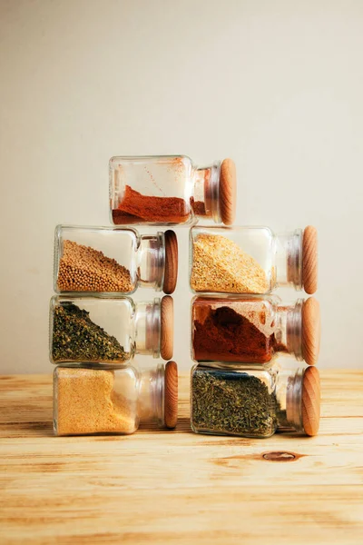 A group of seasonings in glass jars on a light wooden background. Paprika, herbs, mustard, garlic, front view, selective focus