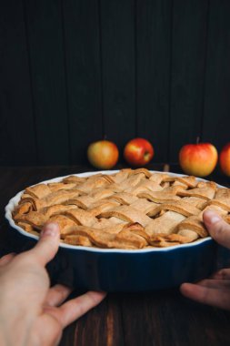 Elmalı turta mavi formda, kadın eli ile koyu ahşap arka planda. Hazır turta. Ön görünüm