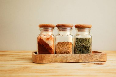 Hafif ahşap arka planda cam kavanozlarda bir grup baharat. Paprika, otlar, hardal, sarımsak, ön manzara, seçici odak