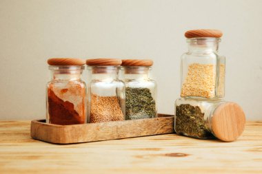 Hafif ahşap arka planda cam kavanozlarda bir grup baharat. Paprika, otlar, hardal, sarımsak, ön manzara, seçici odak