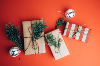 Noel 'i kutlamak, yeni yıl geçmişi. Kahverengi ve kırmızı kağıtlara sarılı hediyeler kırmızı arka planda çam dallarıyla. Üst görünüm