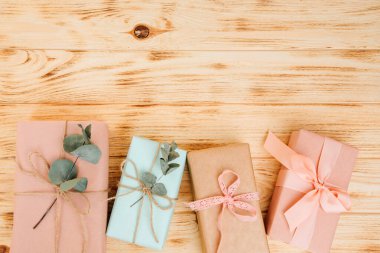 Selamlaşmak için arka plan. Yumuşak pembe ve mavi kağıda sarılı hediyeler, açık ahşap arka planda kuru okaliptüs dallarıyla. Üst görünüm