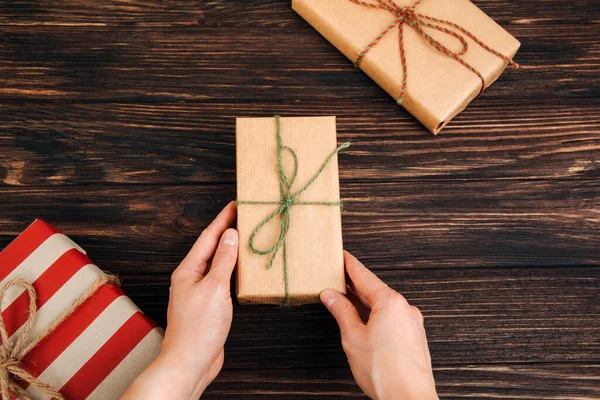 Christmas, festive background. Gifts wrapping in brown paper in womens hand on a dark wooden background. Top view