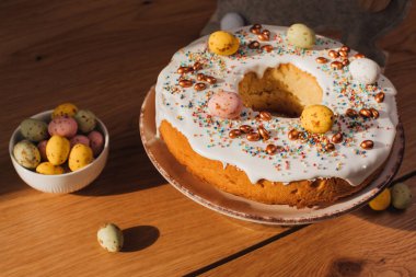 Yuvarlak Paskalya keki, beyaz protein kremi ve mutfaktaki ahşap masaya renkli serpiştirilmiş. Üst görünüm