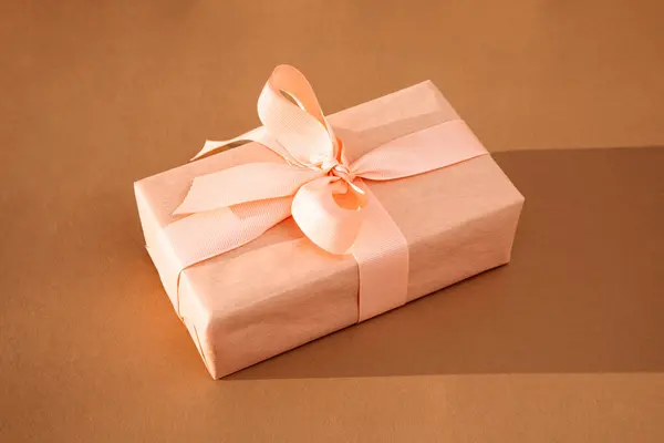 Greeting background. Gift wrapping in soft pink paper on a brown background with copy space. Top view