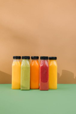 Şeffaf plastik şişelerde meyve ve sebze içecekleri. Kahverengi-yeşil arka planda kırmızı, yeşil, turuncu meyve püresi. Sağlıklı beslenme kavramı. Ön görünüm