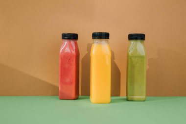 Şeffaf plastik şişelerde meyve ve sebze içecekleri. Kahverengi-yeşil arka planda kırmızı, yeşil, turuncu meyve püresi. Sağlıklı beslenme kavramı. Ön görünüm