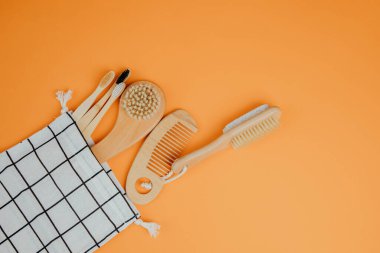 Çevreye dost banyo cihazları kurun. Tahta fırçalar, tarak, turuncu arka planda tekstil torbasında bambu diş fırçaları. Düz yatıyordu