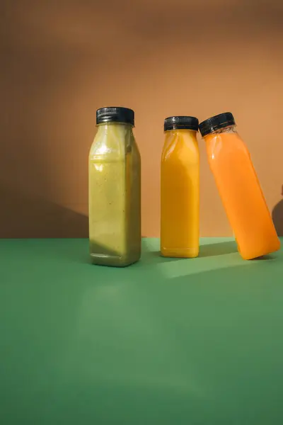 Fruit and vegetable smoothies in transparent plastic bottles. Green, orange smoothies on a brown-green background. The concept of healthy eating. Front view