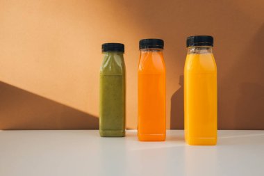 Şeffaf plastik şişelerde meyve ve sebze içecekleri. Kahverengi-beyaz arka planda yeşil, turuncu meyve püresi. Sağlıklı beslenme kavramı. Ön görünüm