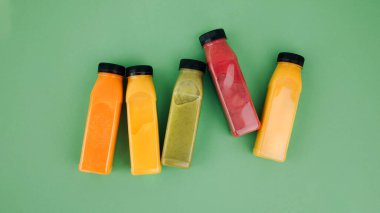 Şeffaf plastik şişelerde meyve ve sebze içecekleri. Yeşil arka planda kırmızı, yeşil, turuncu meyve püresi. Sağlıklı beslenme kavramı. Web afişi. Üst görünüm