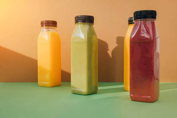 Fruit and vegetable smoothies in transparent plastic bottles. Red, green, orange smoothies on a brown-green background. The concept of healthy eating. Front view