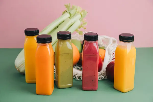 Fruit and vegetable smoothies in transparent plastic bottles. Green, red, orange smoothies on a pink-green background with avocado, apples and celery. The concept of healthy eating. Front view