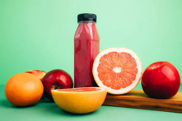 Fruit and vegetable smoothies in transparent plastic bottles. Red smoothie on a green background with oranges, apples and grapefruit. The concept of healthy eating. Front view