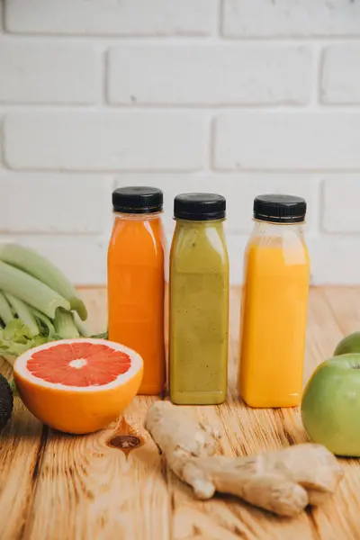 Fruit and vegetable smoothies in transparent plastic bottles. Green, orange smoothies on a wooden table. The concept of healthy eating. Front view