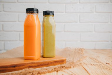 Şeffaf plastik şişelerde meyve ve sebze içecekleri. Ahşap bir masada yeşil, turuncu meyve püresi. Sağlıklı beslenme kavramı. Ön görünüm