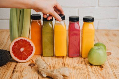 Şeffaf plastik şişelerde meyve ve sebze içecekleri. Kırmızı, yeşil, turuncu meyve suları, kadın eli olan ahşap bir masada. Sağlıklı beslenme kavramı. Ön görünüm