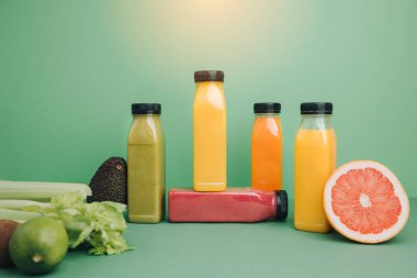 Şeffaf plastik şişelerde meyve ve sebze içecekleri. Avokado, elma ve kereviz ile yeşil arka planda yeşil, kırmızı, turuncu smoothie. Sağlıklı beslenme kavramı. Ön görünüm