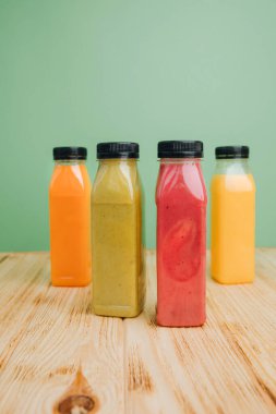 Şeffaf plastik şişelerde meyve ve sebze içecekleri. Yeşil, kırmızı, turuncu meyve suları yeşil ve ahşap arka planda. Sağlıklı beslenme kavramı. Ön görünüm