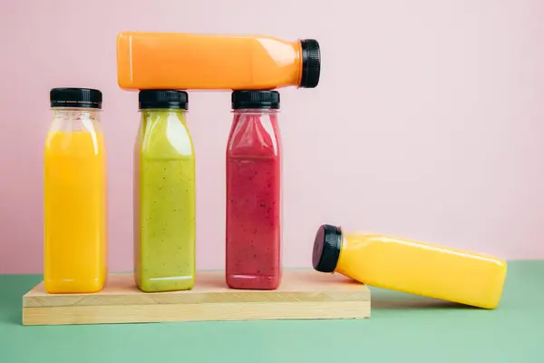 Fruit and vegetable smoothies in transparent plastic bottles. Green, red, orange smoothies on a pink-green background. The concept of healthy eating. Front view