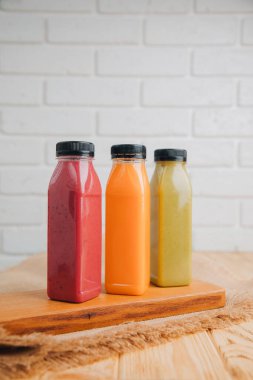 Şeffaf plastik şişelerde meyve ve sebze içecekleri. Tahta bir masada yeşil, turuncu ve kırmızı meyve püresi. Sağlıklı beslenme kavramı. Ön görünüm
