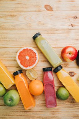 Şeffaf plastik şişelerde meyve ve sebze içecekleri. Ahşap bir masada kırmızı, yeşil, turuncu meyve püresi. Sağlıklı beslenme kavramı. Üst görünüm