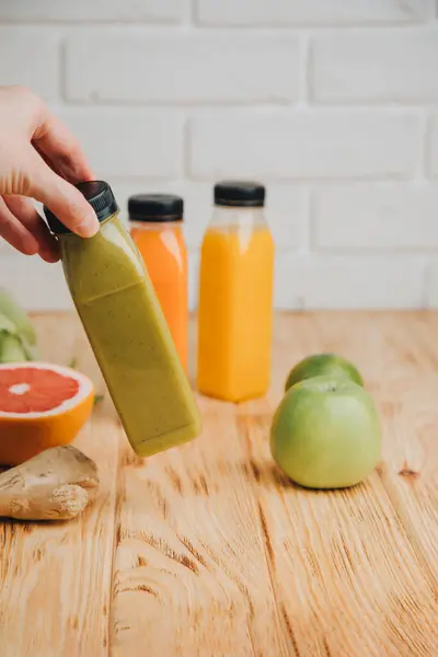 Fruit and vegetable smoothies in transparent plastic bottles. Red, green, orange smoothies on a wooden table with womens hand. The concept of healthy eating. Front view