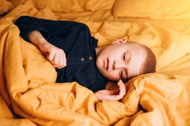 Neşeli bir çocuk sarı köşede yatıyor ve yüzünü çeviriyor. Kötü durumdaki çocuk. Ön görünüm