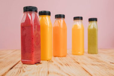 Şeffaf plastik şişelerde meyve ve sebze içecekleri. Ahşap bir masada kırmızı, yeşil, turuncu meyve püresi. Sağlıklı beslenme kavramı. Ön görünüm