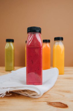 Şeffaf plastik şişelerde meyve ve sebze içecekleri. Ahşap bir masada kırmızı, yeşil, turuncu meyve püresi. Sağlıklı beslenme kavramı. Ön görünüm