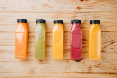 Şeffaf plastik şişelerde meyve ve sebze içecekleri. Ahşap bir masada kırmızı, yeşil, turuncu meyve püresi. Sağlıklı beslenme kavramı. Üst görünüm
