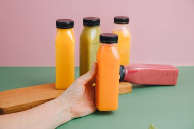 Şeffaf plastik şişelerde meyve ve sebze içecekleri. Yeşil, kırmızı, turuncu smoothie pembe-yeşil arka planda. Sağlıklı beslenme kavramı. Ön görünüm