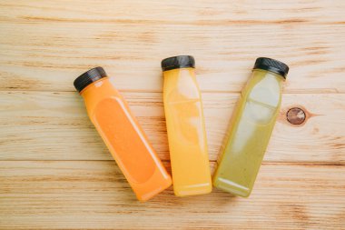 Şeffaf plastik şişelerde meyve ve sebze içecekleri. Ahşap bir masada kırmızı, yeşil, turuncu meyve püresi. Sağlıklı beslenme kavramı. Üst görünüm