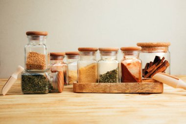 Hafif ahşap arka planda cam kavanozlarda bir grup baharat. Paprika, otlar, hardal, sarımsak, ön manzara, seçici odak