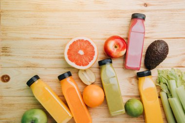Şeffaf plastik şişelerde meyve ve sebze içecekleri. Ahşap bir masada kırmızı, yeşil, turuncu meyve püresi. Sağlıklı beslenme kavramı. Üst görünüm