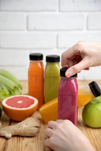 Fruit and vegetable smoothies in transparent plastic bottles. Red, green, orange smoothies with female hands on a wooden table. The concept of healthy eating. Front view