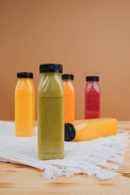 Şeffaf plastik şişelerde meyve ve sebze içecekleri. Kahverengi ve ahşap arka planda yeşil, kırmızı, turuncu meyve püresi. Sağlıklı beslenme kavramı. Ön görünüm