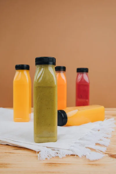 Fruit and vegetable smoothies in transparent plastic bottles. Green, red, orange smoothies on a brown and wooden background. The concept of healthy eating. Front view