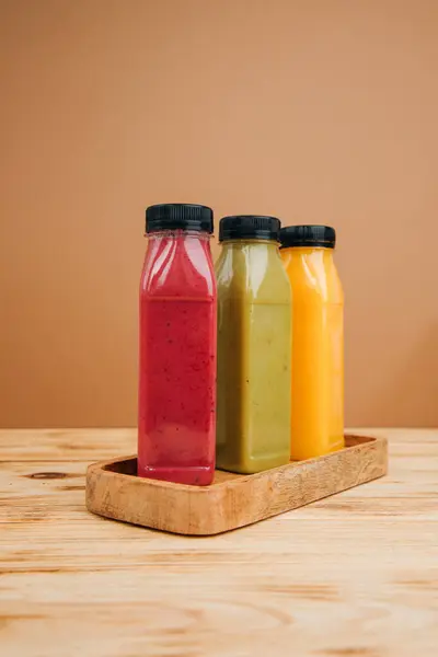 Fruit and vegetable smoothies in transparent plastic bottles. Green, red, orange smoothies on a brown and wooden background. The concept of healthy eating. Front view