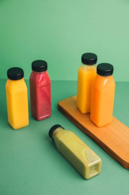 Şeffaf plastik şişelerde meyve ve sebze içecekleri. Yeşil, kırmızı, turuncu içecekler yeşil arka planda. Sağlıklı beslenme kavramı. Üst görünüm