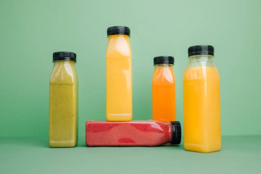 Şeffaf plastik şişelerde meyve ve sebze içecekleri. Yeşil, kırmızı, turuncu içecekler yeşil arka planda. Sağlıklı beslenme kavramı. Ön görünüm