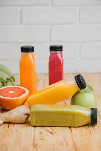 Fruit and vegetable smoothies in transparent plastic bottles. Green, orange, red smoothies on a wooden table. The concept of healthy eating. Front view